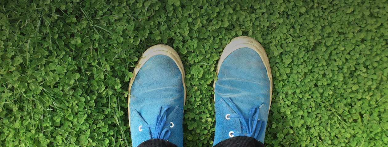 footer image showing two feet in blue shoes standing on green clover